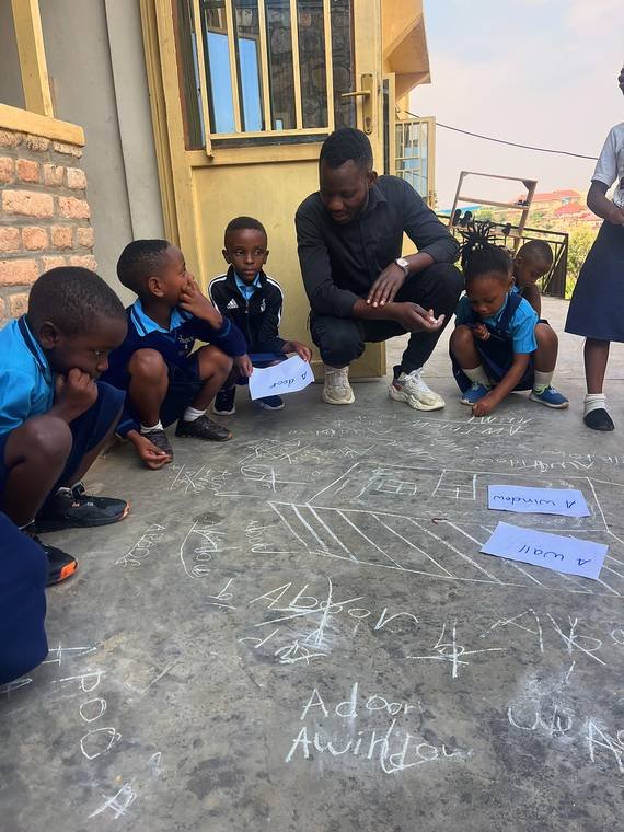 A teacher and children crouched over a chalk drawing and word cards outside a classroom