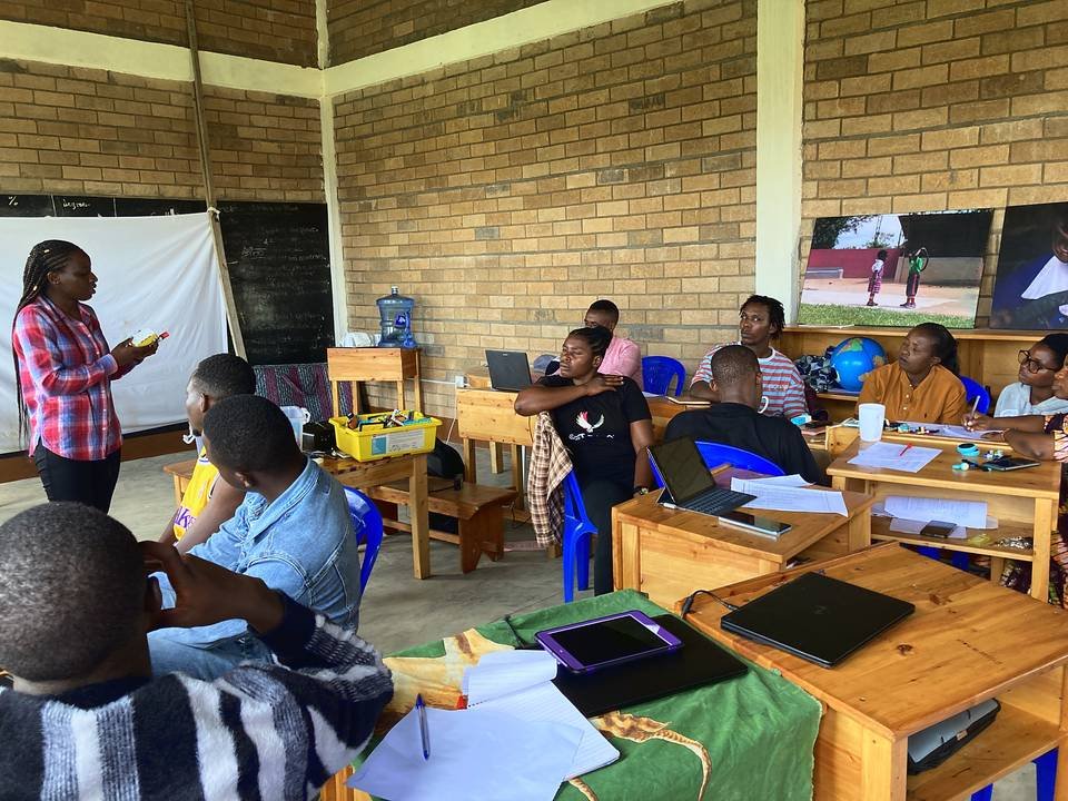 A facilitator addressing teachers seated at group tables in a brick classroom