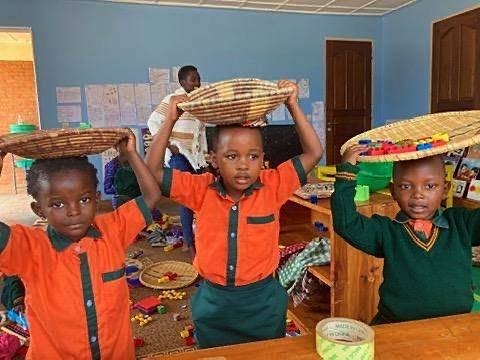 Three learners smiling with woven baskets of learning materials on their heads