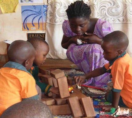 Children building with wooden blocks beside their teacher