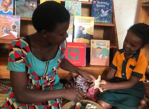 A teacher reading with a learner beside the library bookshelves