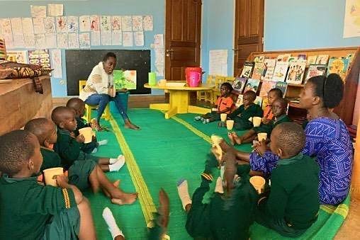 Learners sitting in a circle on a green mat with cups during circle time