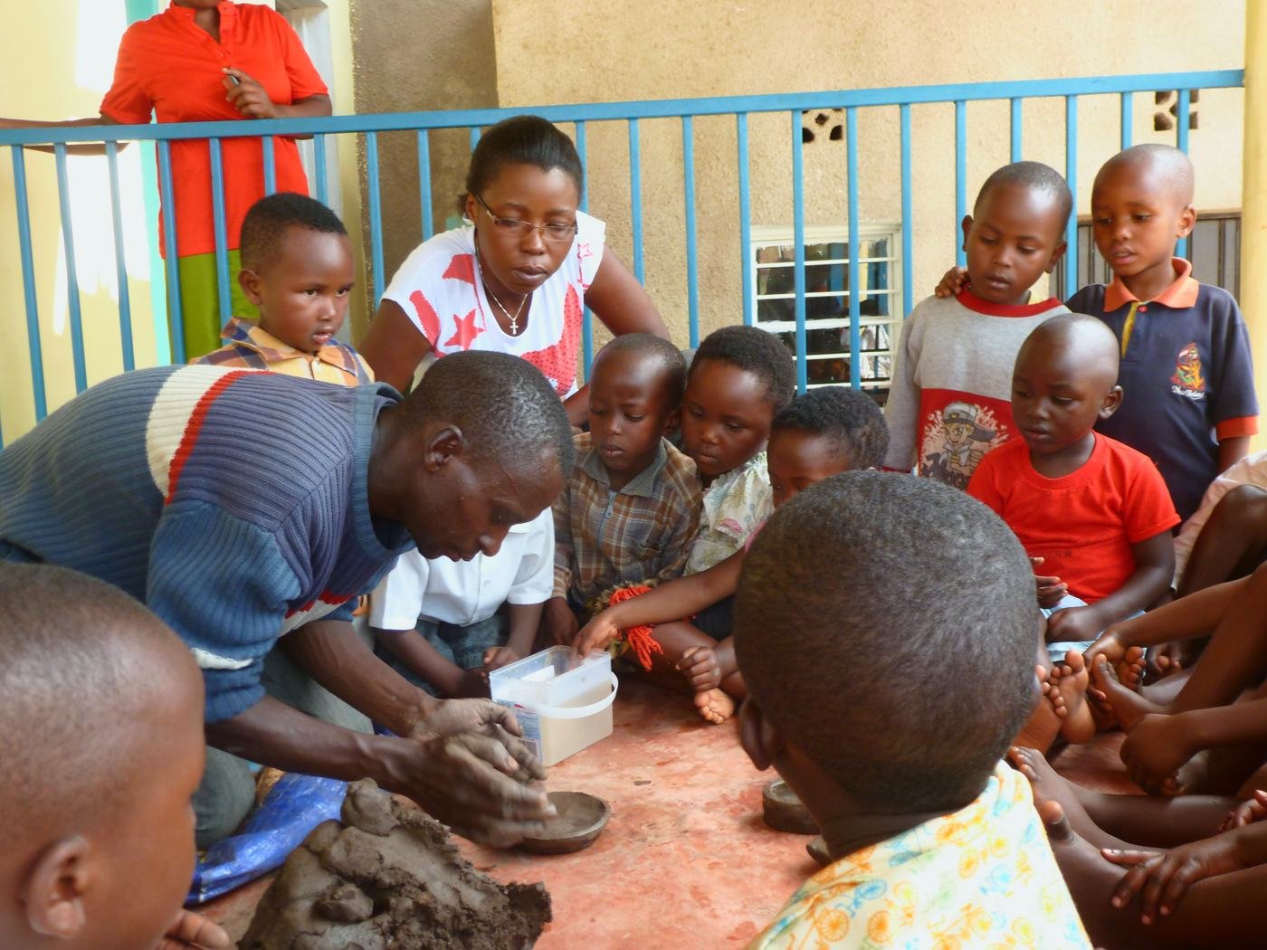 Louise Batamuriza and a colleague showing young children how to shape a clay bowl