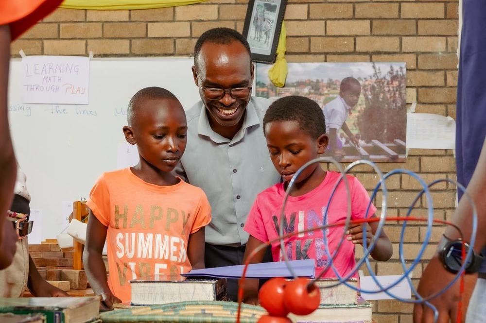 A teacher working through a maths activity with two learners under a Learning Math Through Play display