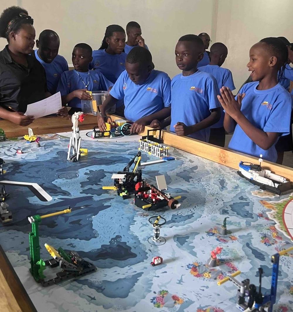 A TEACH Rwanda robotics team in branded shirts working on builds around an ocean-themed competition mat