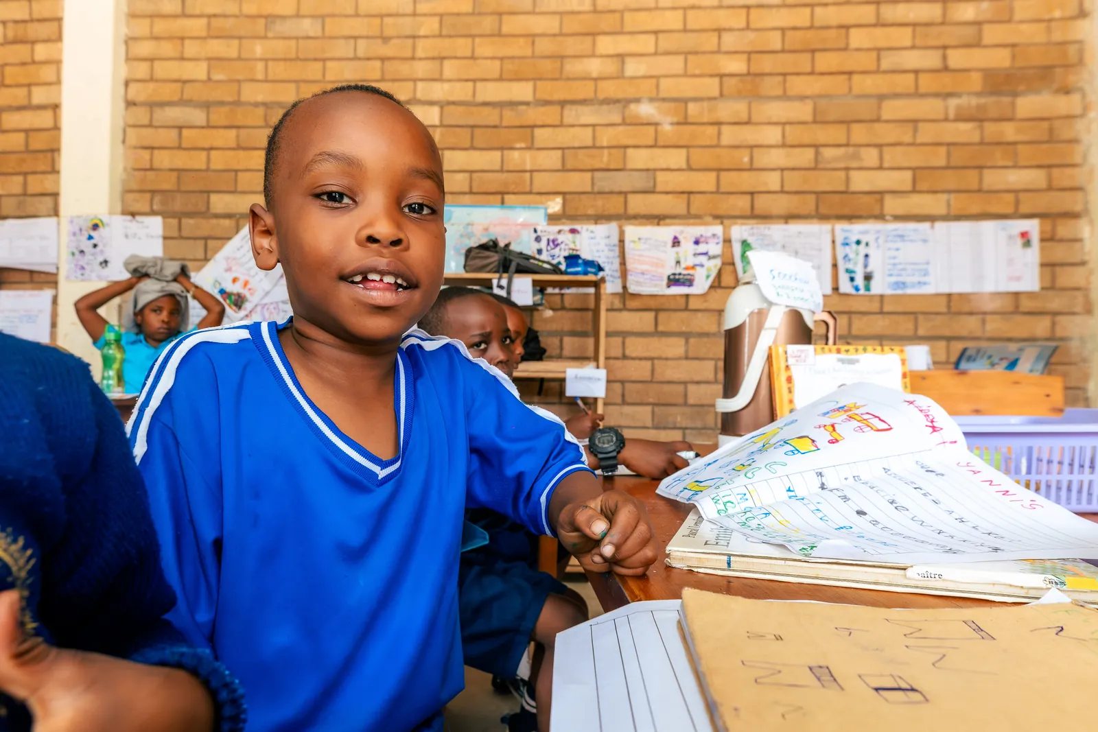 A boy in a blue top smiling at the camera in a classroom