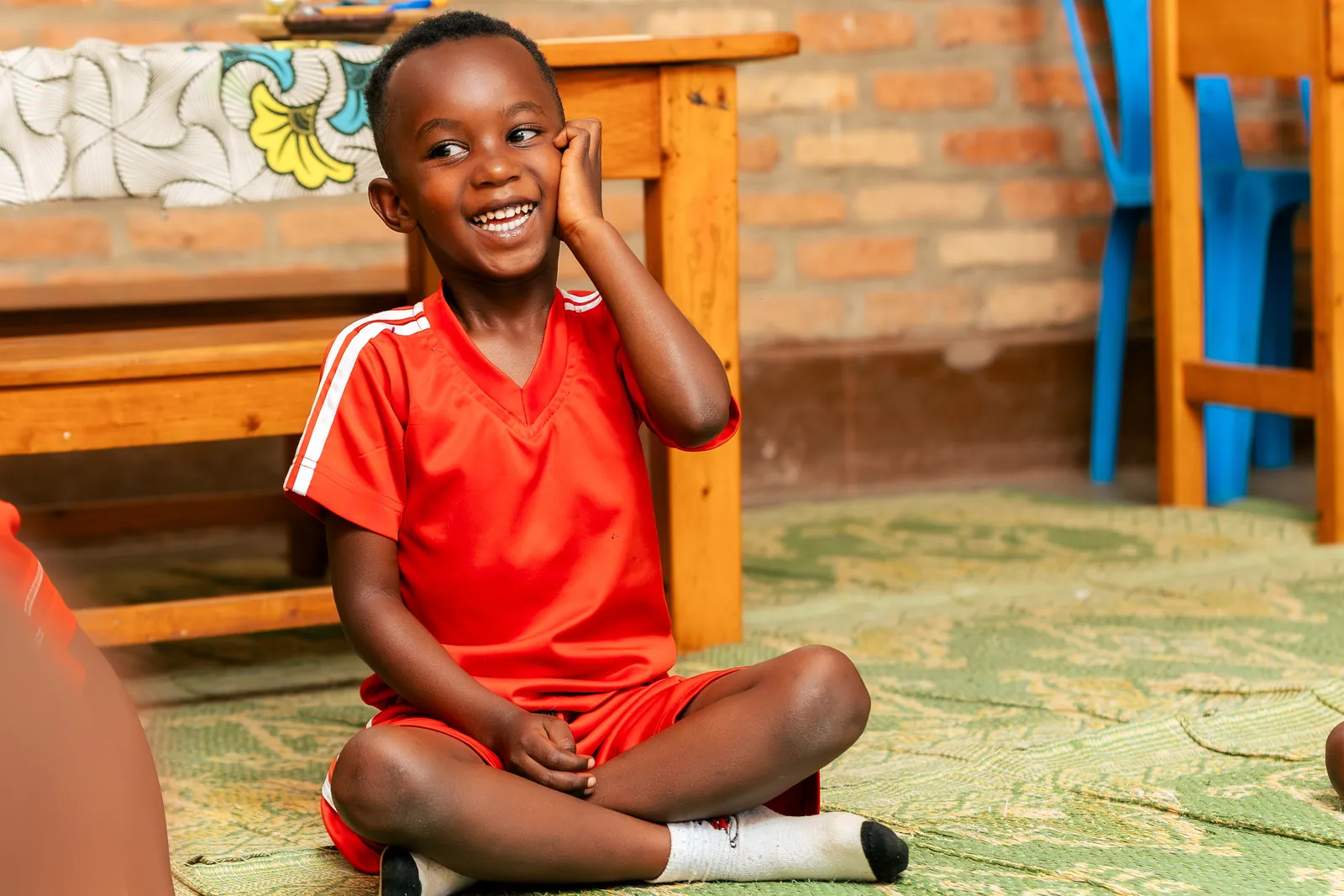 A boy smiling with his hand against his cheek, sitting cross-legged