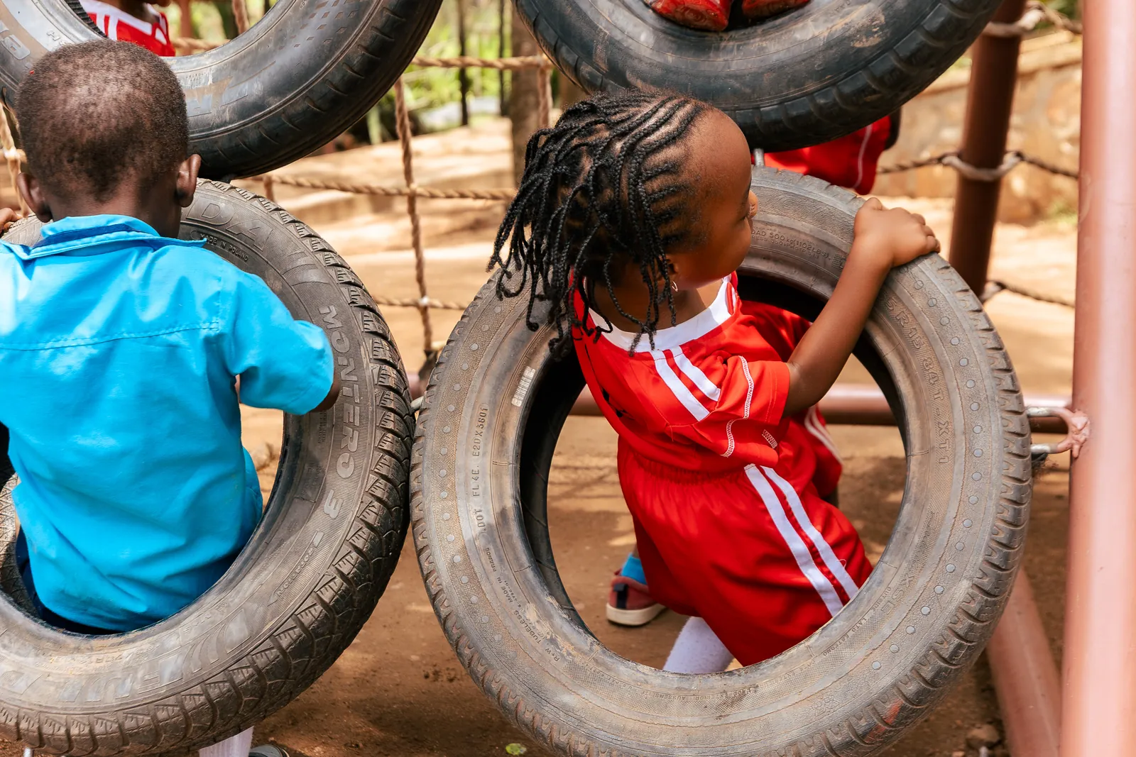 A child in a red kit climbing through a playground tyre