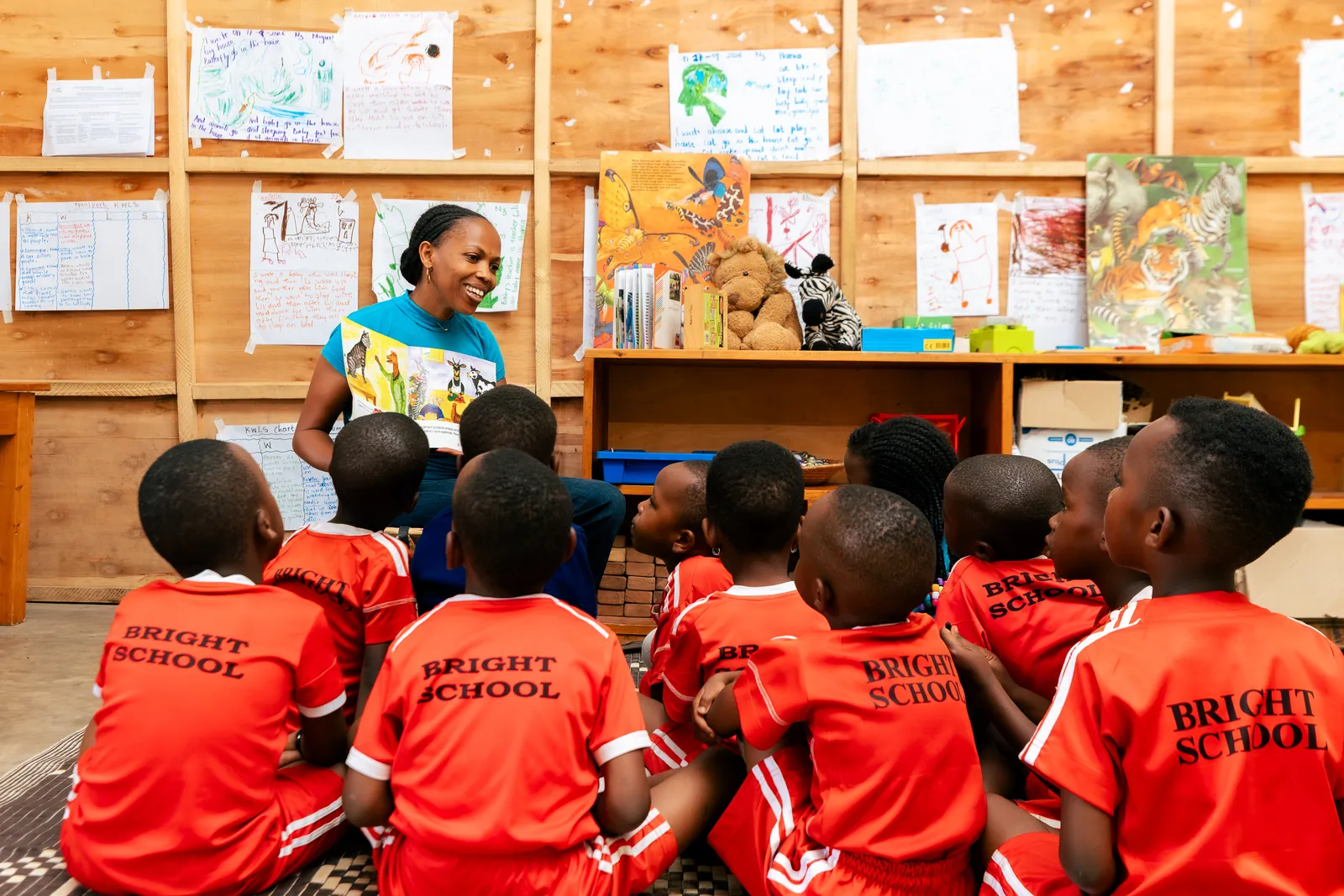 Children seated on a mat watching a teacher read aloud