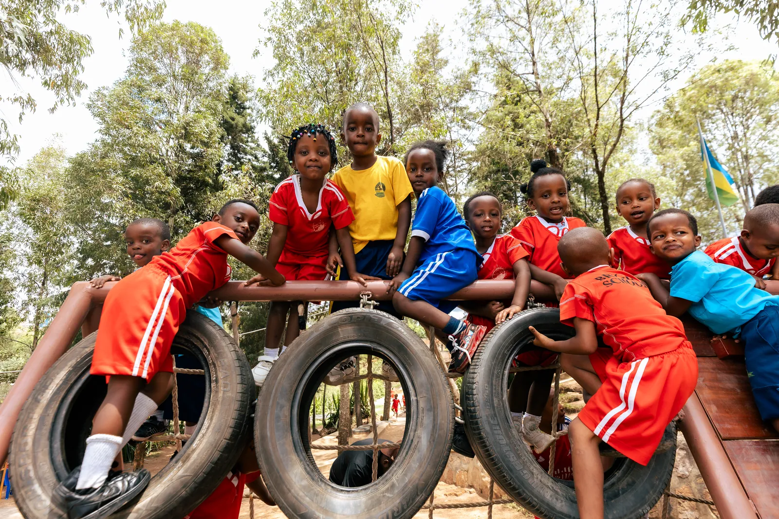 A group of children in red and blue climbing and smiling on the tyre wall