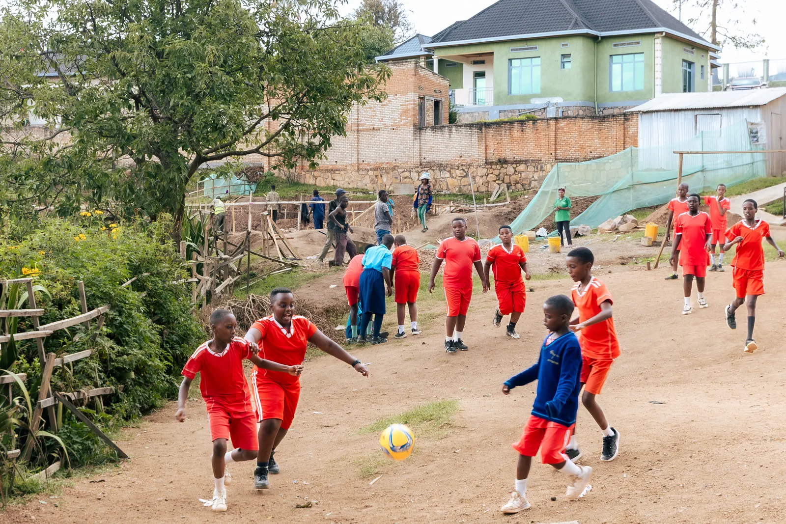Children in red playing football on a dirt pitch