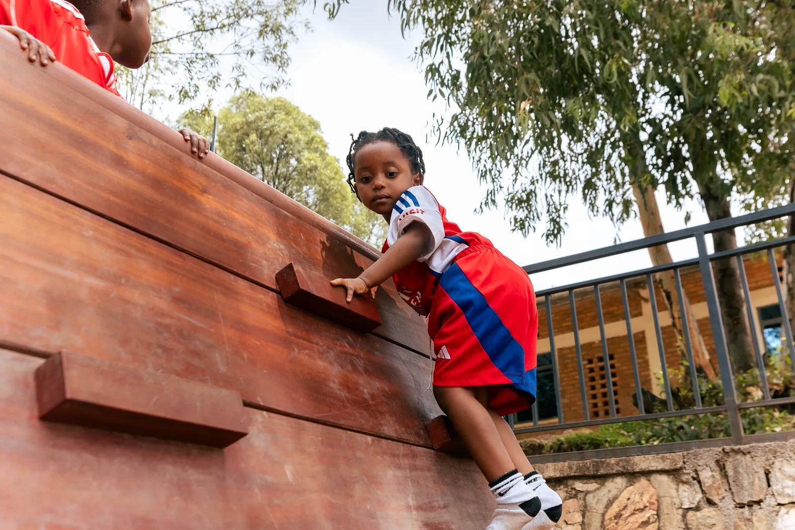 A girl smiling at the camera as she climbs the wooden wall