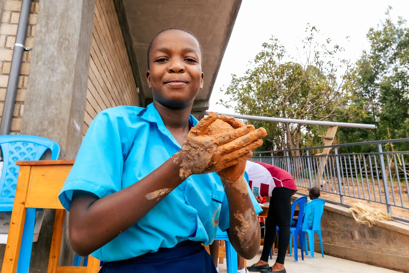 A girl in a light blue shirt smiling and holding clay in her hands
