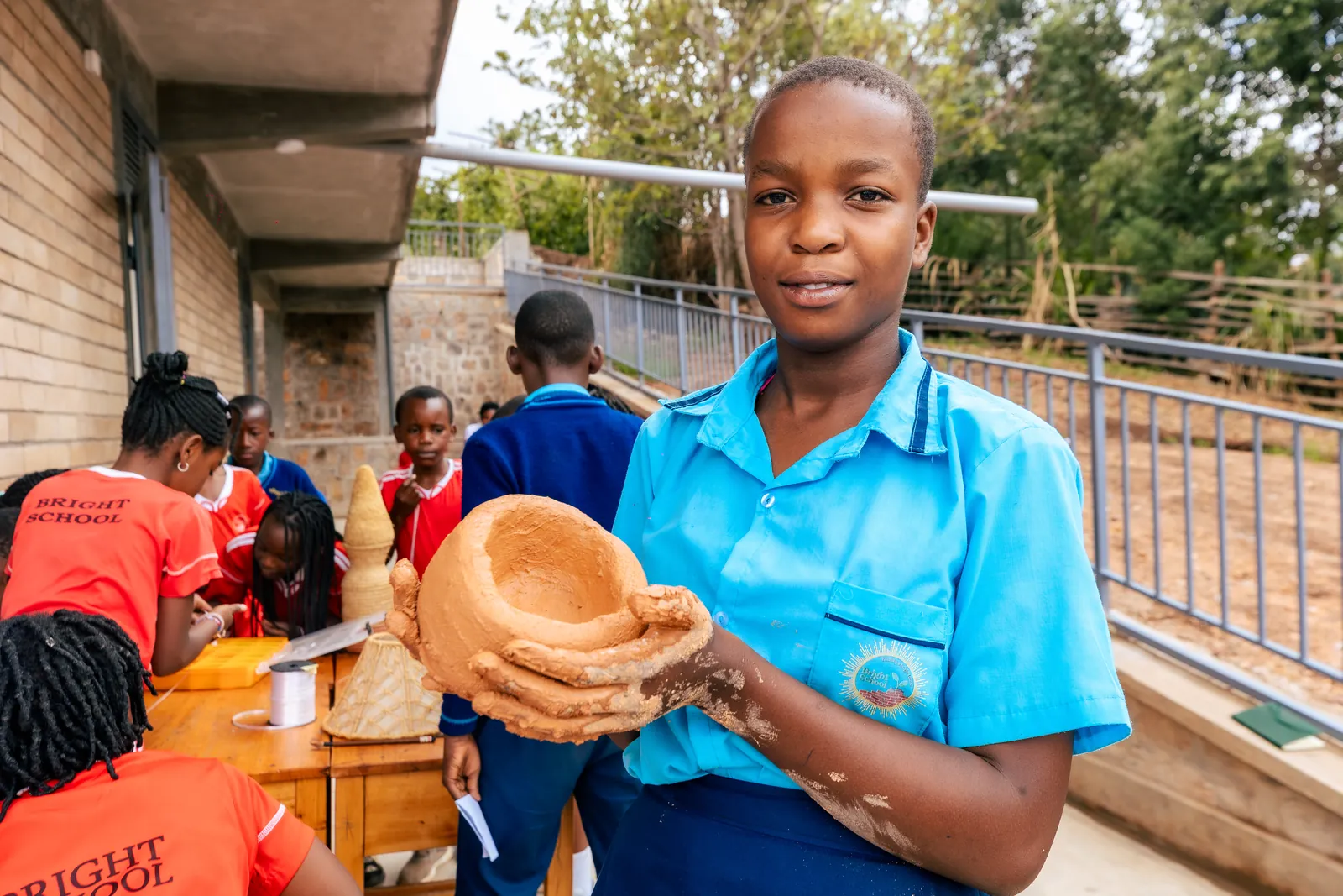 A smiling girl in a light blue shirt showing the clay bowl she made