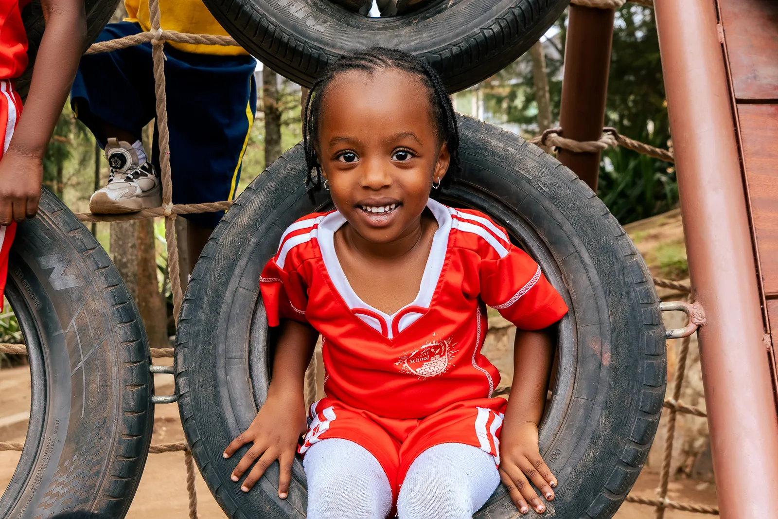 A girl in red sports kit smiling at the camera from inside a playground tyre