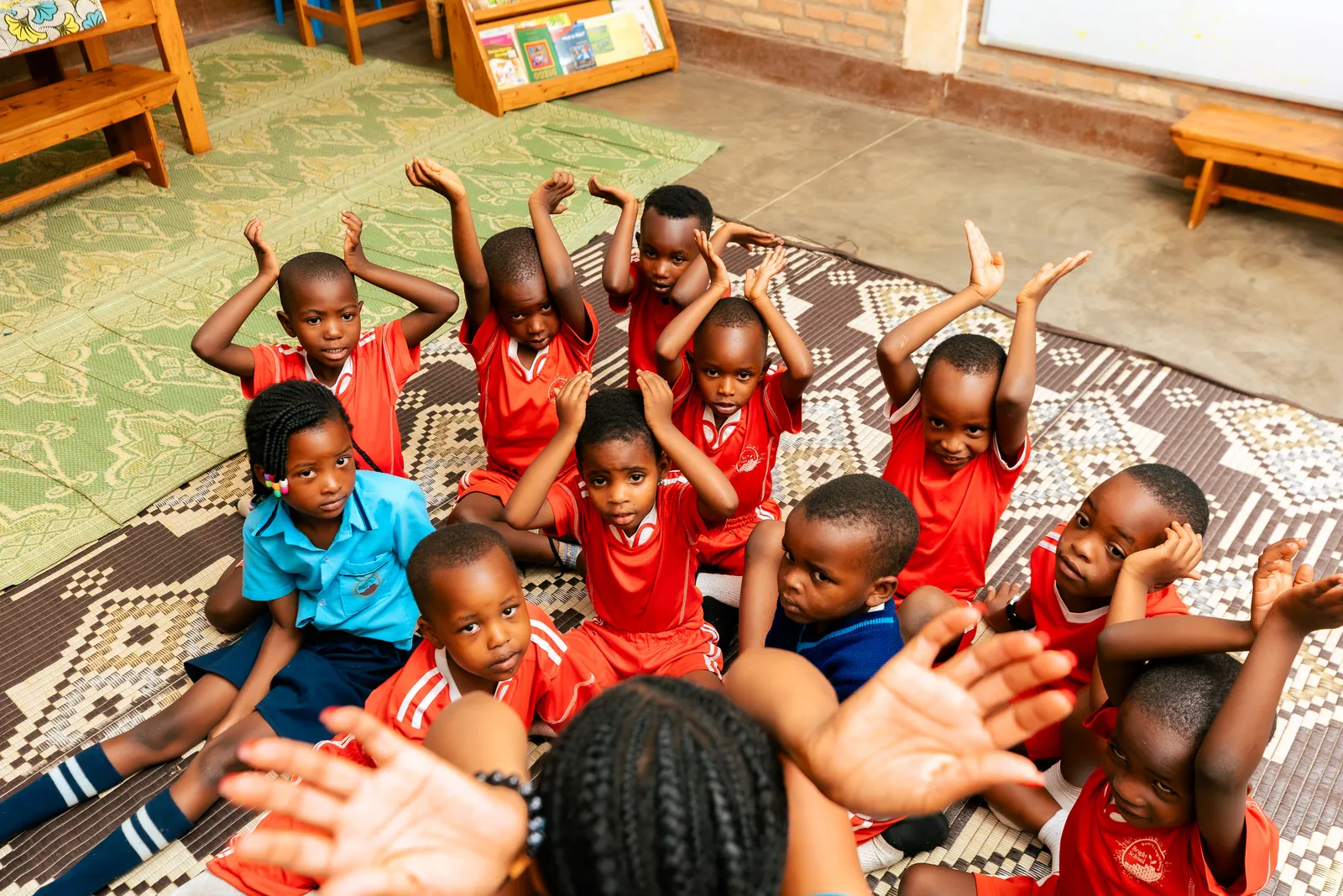 A class of children on a rug with their hands raised in the air