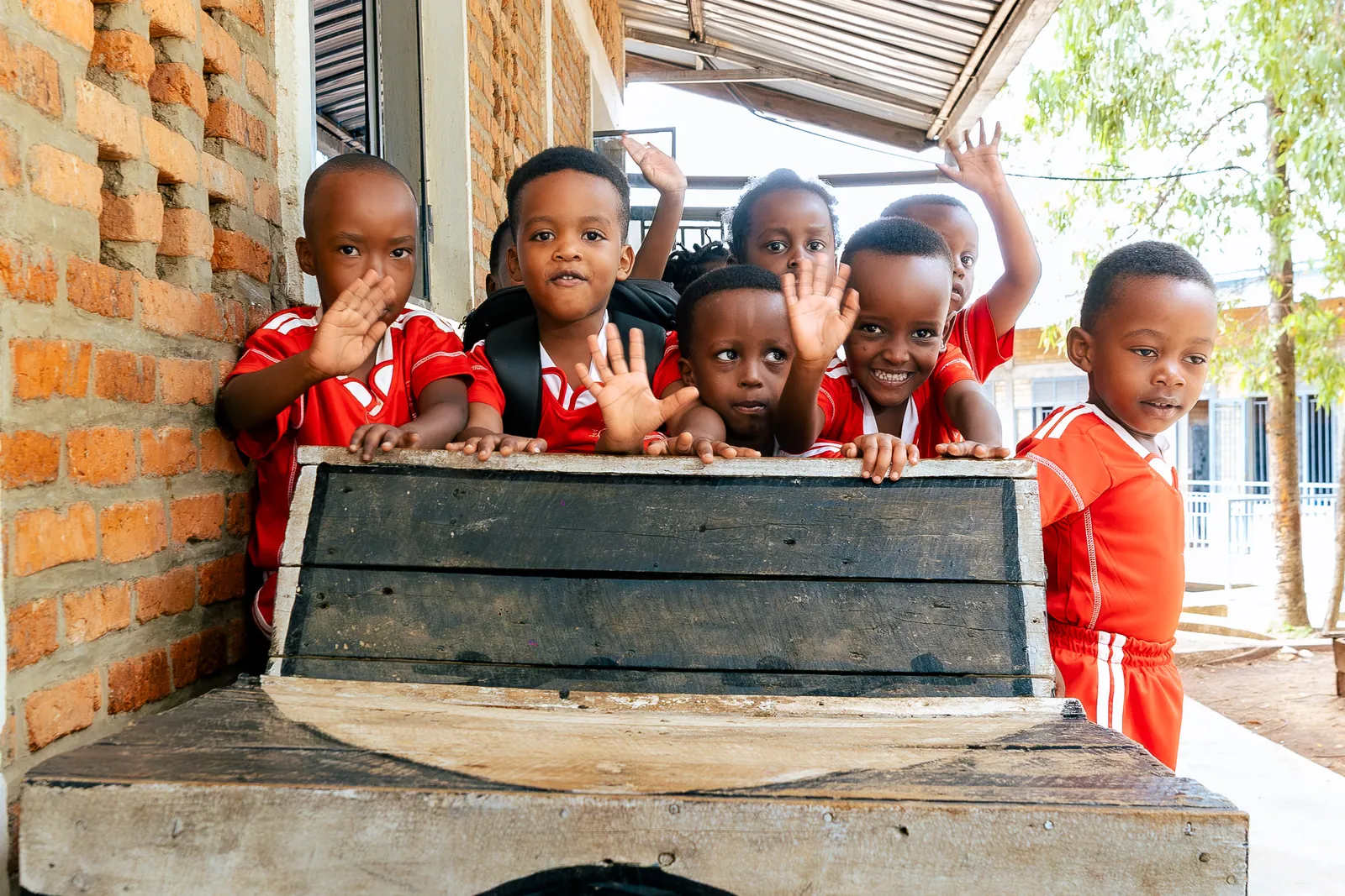 Children in red kits waving from behind a painted wooden bench