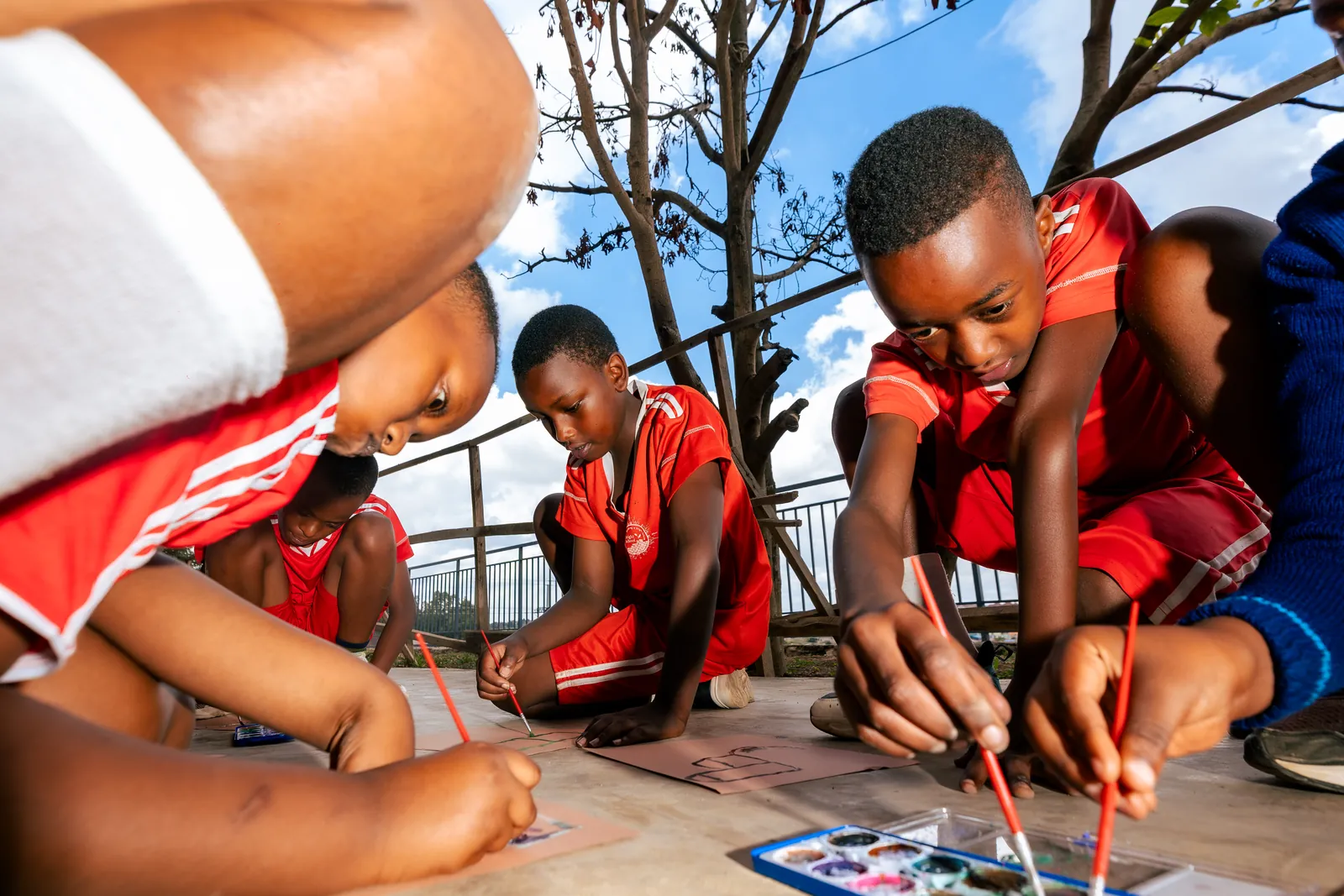 Children painting on the floor of a terrace, shot from a low angle under blue sky