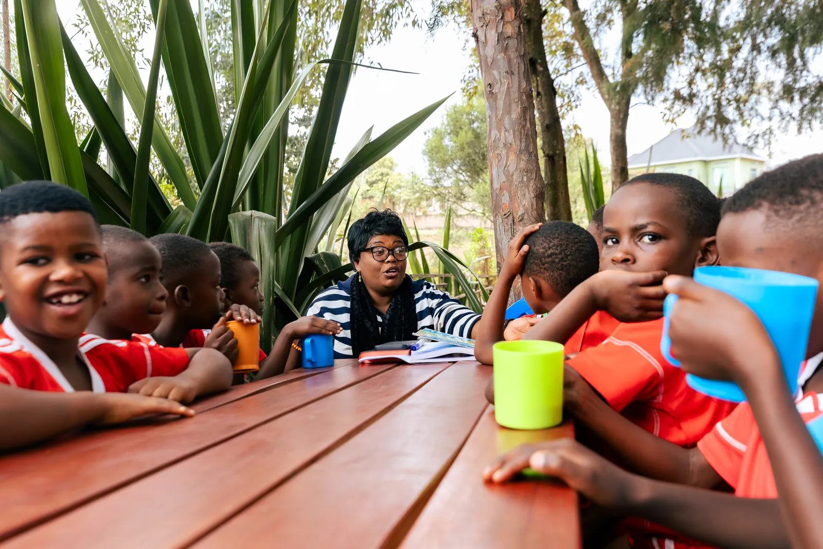 Children in red kits smiling over cups at an outdoor snack table