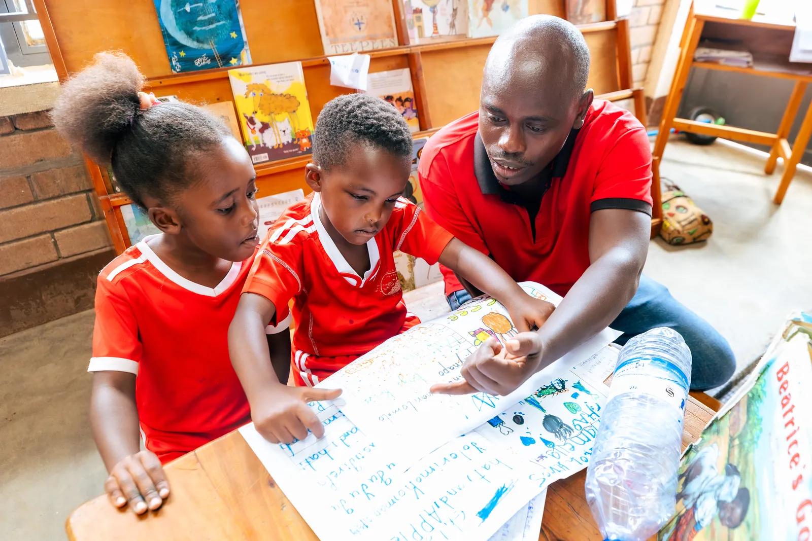 A teacher kneeling with two girls as they fill in a worksheet together