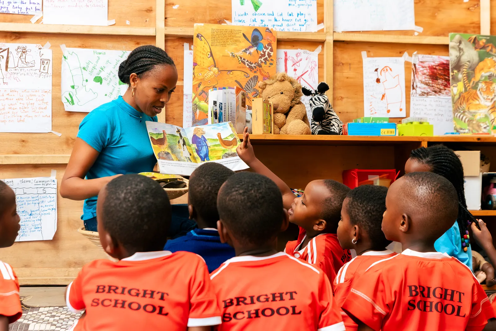 A teacher in a turquoise top reading to children in Bright School shirts