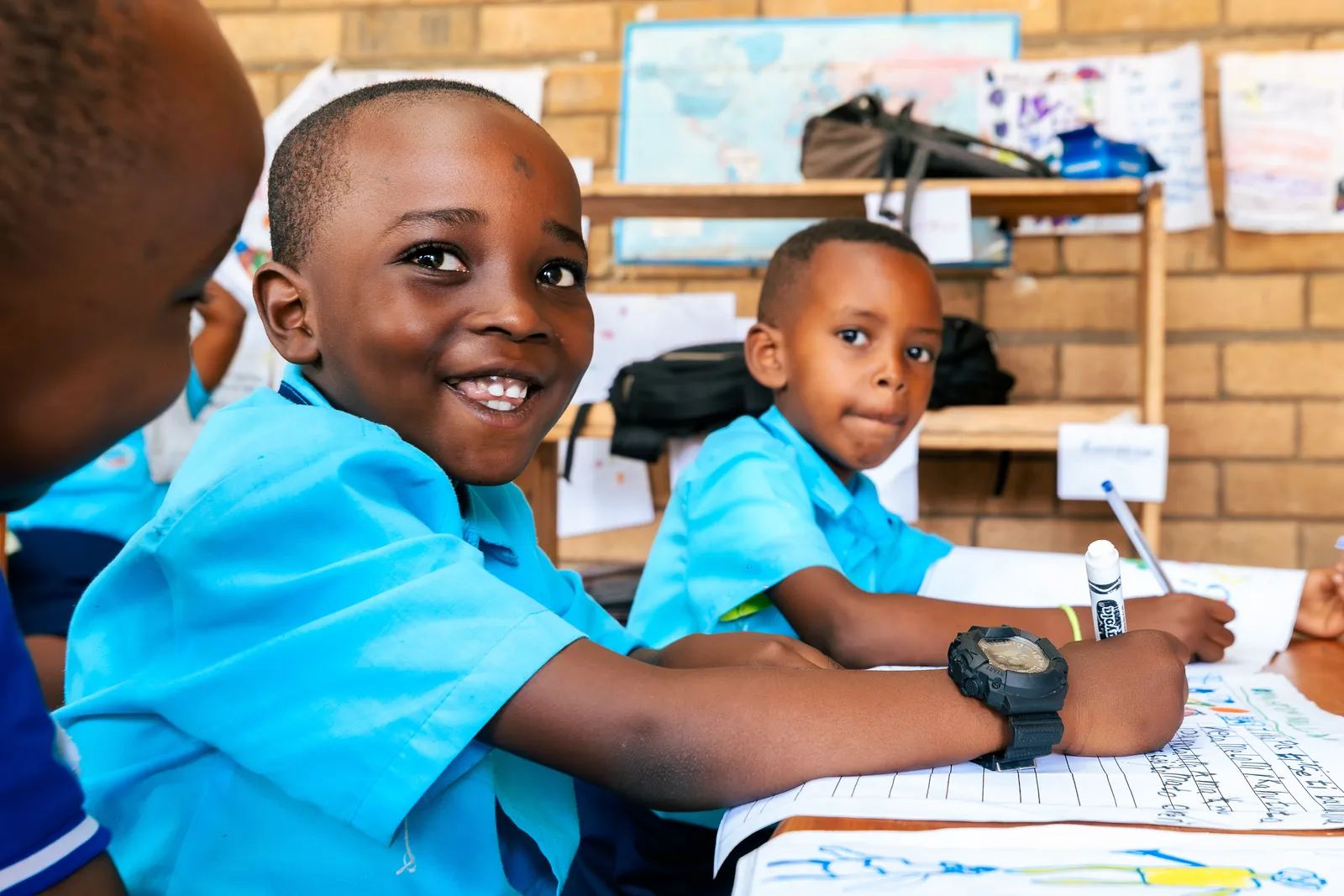 Two boys writing side by side, one smiling at the camera